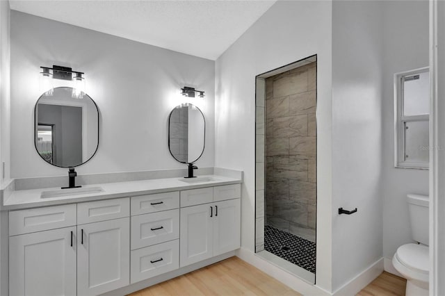 full bathroom featuring double vanity, toilet, a sink, wood finished floors, and tiled shower