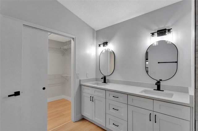 bathroom featuring double vanity, a textured ceiling, a sink, and wood finished floors