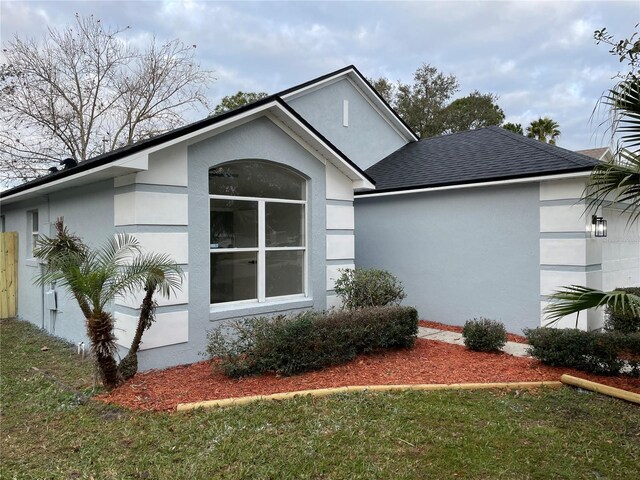 view of side of property featuring roof with shingles, a lawn, and stucco siding