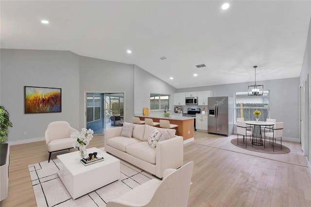 living area featuring light wood-type flooring, an inviting chandelier, lofted ceiling, and recessed lighting