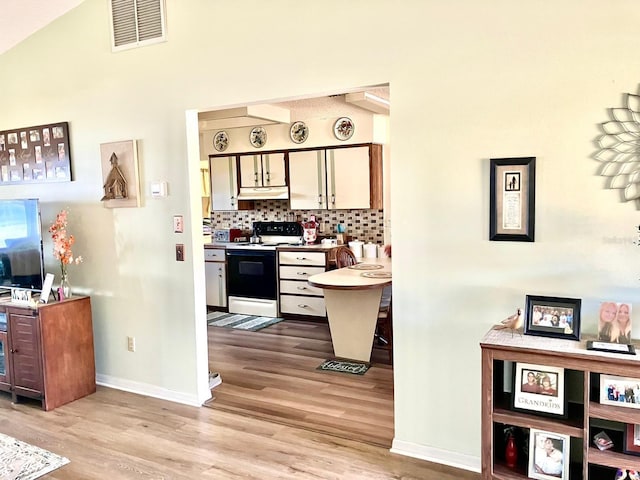 kitchen featuring lofted ceiling, electric range, light hardwood / wood-style floors, and decorative backsplash