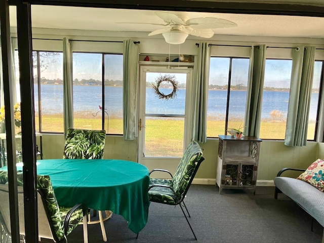 sunroom with ceiling fan and a water view