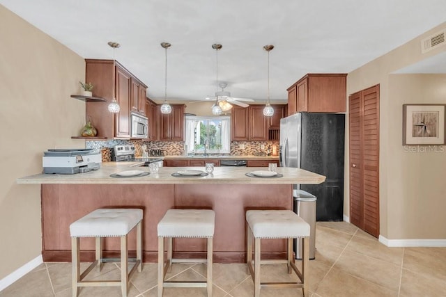 kitchen with kitchen peninsula, appliances with stainless steel finishes, tasteful backsplash, light tile patterned flooring, and pendant lighting