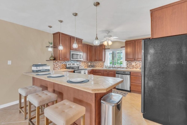 kitchen with appliances with stainless steel finishes, decorative light fixtures, kitchen peninsula, a breakfast bar, and light tile patterned floors