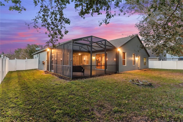 back house at dusk featuring glass enclosure and a lawn