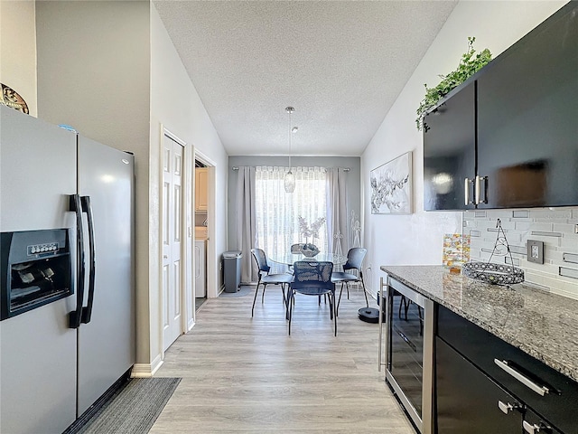 kitchen with decorative light fixtures, vaulted ceiling, stainless steel refrigerator with ice dispenser, dark stone counters, and beverage cooler