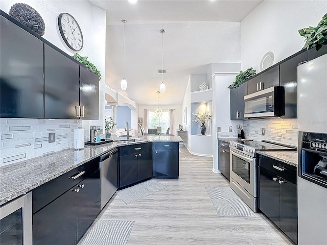 kitchen featuring decorative backsplash, sink, hanging light fixtures, light wood-type flooring, and stainless steel appliances