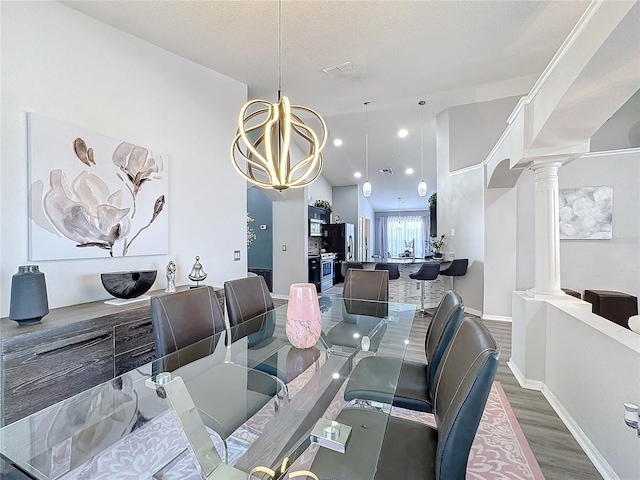 dining room featuring an inviting chandelier, wood-type flooring, ornate columns, and a textured ceiling