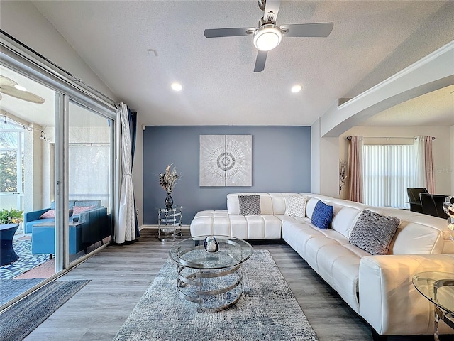 living room with ceiling fan, wood-type flooring, vaulted ceiling, and a textured ceiling