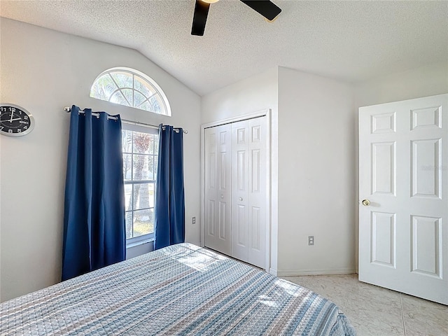 unfurnished bedroom with ceiling fan, vaulted ceiling, light tile patterned flooring, a textured ceiling, and a closet