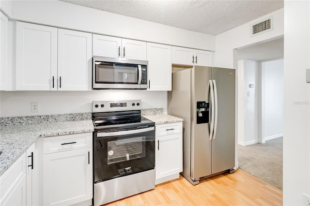 kitchen with appliances with stainless steel finishes, light colored carpet, white cabinets, and light stone countertops