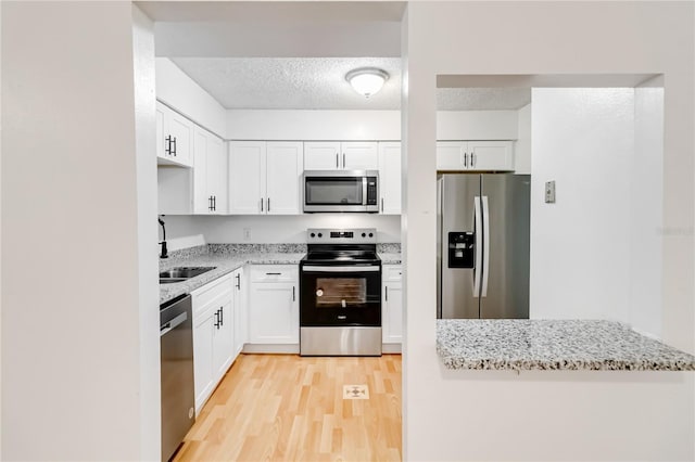 kitchen featuring sink, light stone countertops, appliances with stainless steel finishes, a textured ceiling, and white cabinets