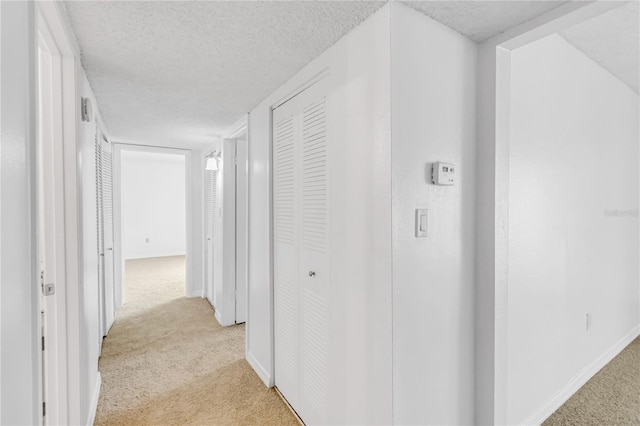 hall with light colored carpet and a textured ceiling