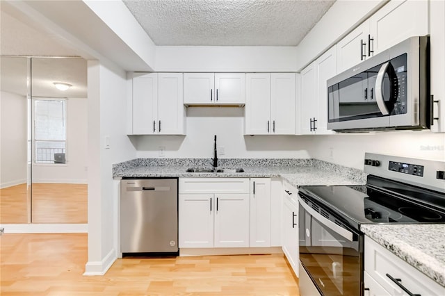 kitchen featuring appliances with stainless steel finishes, white cabinetry, sink, light hardwood / wood-style floors, and a textured ceiling