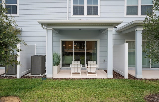 view of exterior entry with central AC unit, a lawn, and a patio