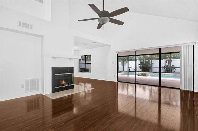 unfurnished living room featuring hardwood / wood-style floors, a towering ceiling, a healthy amount of sunlight, and ceiling fan