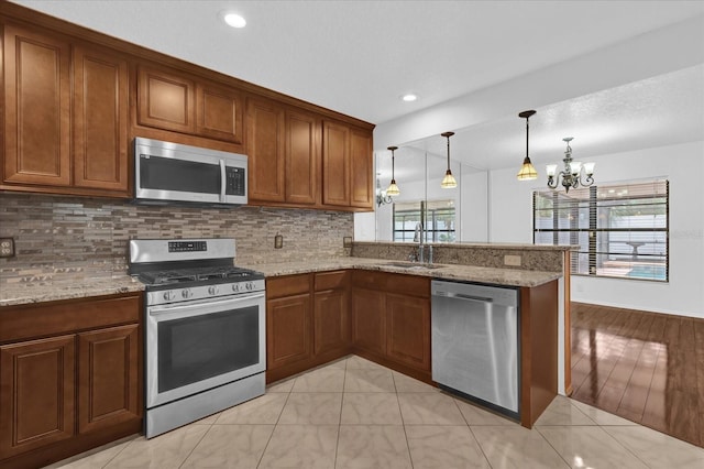 kitchen featuring sink, appliances with stainless steel finishes, hanging light fixtures, light stone countertops, and kitchen peninsula