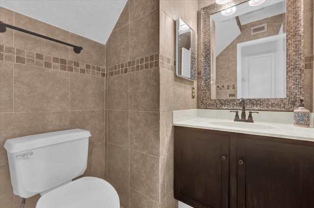 bathroom with lofted ceiling, toilet, tile walls, and vanity