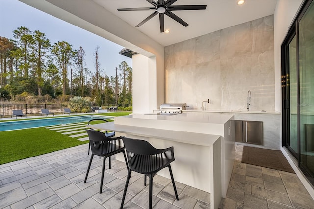 view of patio with ceiling fan, an outdoor bar, a fenced in pool, and area for grilling