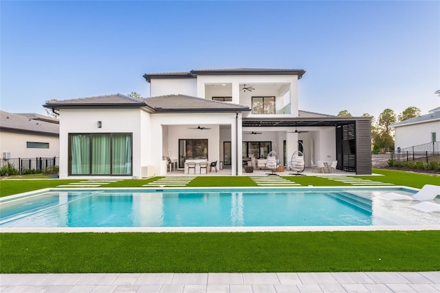 back of house featuring ceiling fan, a fenced in pool, a lawn, and a patio