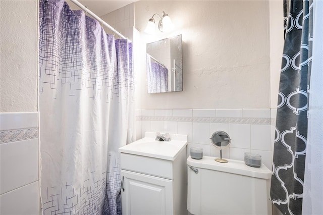 bathroom featuring walk in shower, vanity, toilet, and tile walls