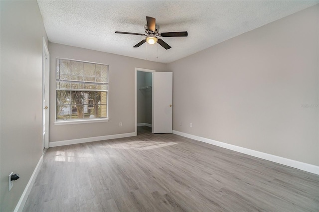 unfurnished bedroom featuring light hardwood / wood-style flooring, a spacious closet, ceiling fan, a textured ceiling, and a closet