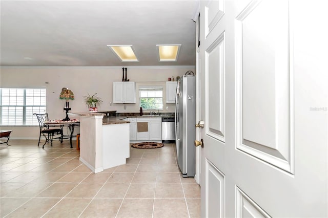 kitchen with white cabinets, appliances with stainless steel finishes, kitchen peninsula, and light tile patterned flooring