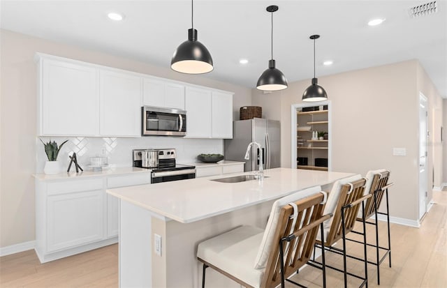 kitchen with appliances with stainless steel finishes, sink, white cabinets, and an island with sink