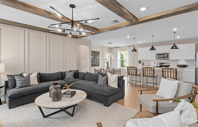 living room with an inviting chandelier, beam ceiling, and light wood-type flooring