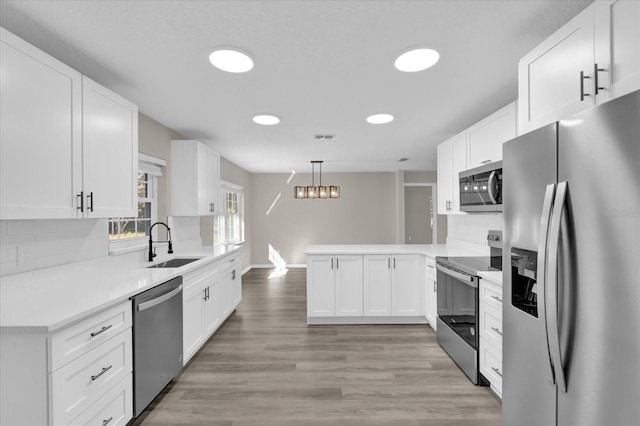 kitchen with kitchen peninsula, sink, white cabinetry, hanging light fixtures, and appliances with stainless steel finishes