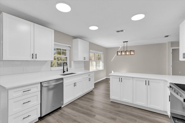 kitchen featuring kitchen peninsula, stainless steel appliances, white cabinets, and decorative light fixtures