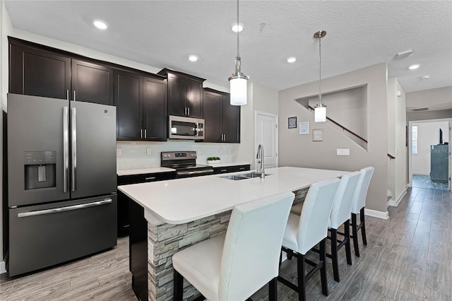 kitchen with sink, a center island with sink, appliances with stainless steel finishes, a kitchen breakfast bar, and pendant lighting