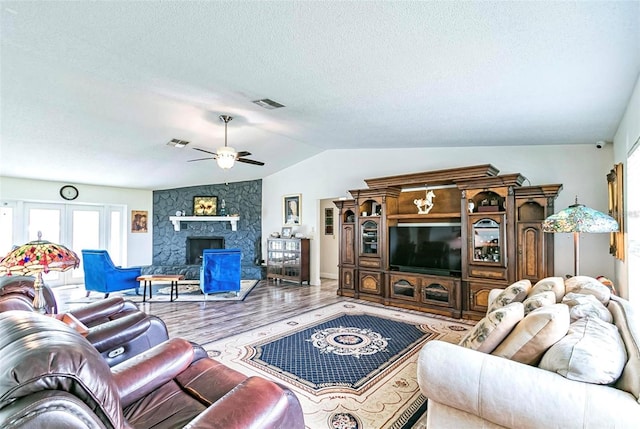 living room featuring a textured ceiling, lofted ceiling, wood-type flooring, a stone fireplace, and ceiling fan