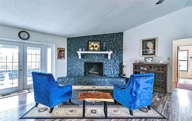 living room featuring vaulted ceiling, a fireplace, wood-type flooring, french doors, and a textured ceiling