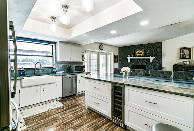 kitchen with sink, appliances with stainless steel finishes, white cabinets, dark stone counters, and beverage cooler