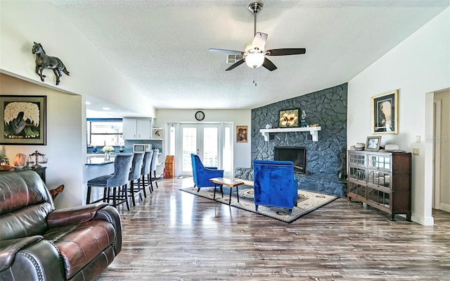 living room with ceiling fan, vaulted ceiling, hardwood / wood-style floors, a stone fireplace, and a textured ceiling