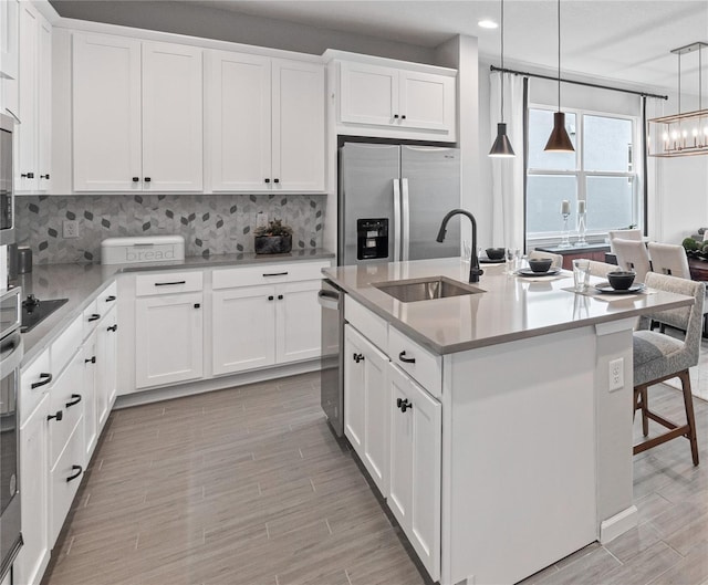 kitchen featuring an island with sink, sink, stainless steel appliances, and white cabinetry