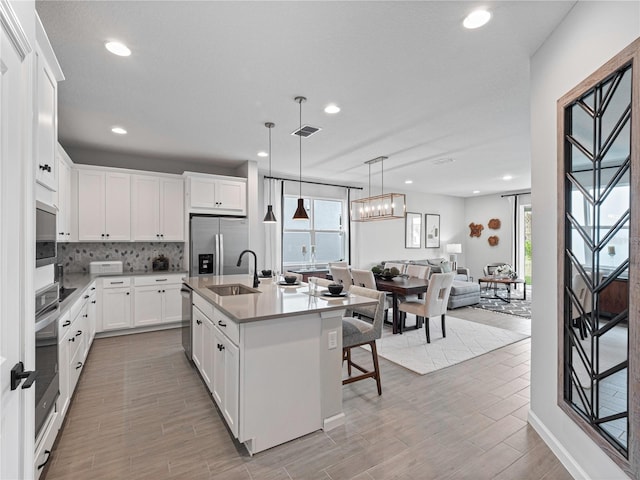 kitchen with pendant lighting, appliances with stainless steel finishes, white cabinetry, sink, and a kitchen island with sink