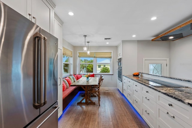 kitchen with breakfast area, dark hardwood / wood-style flooring, appliances with stainless steel finishes, white cabinetry, and dark stone counters