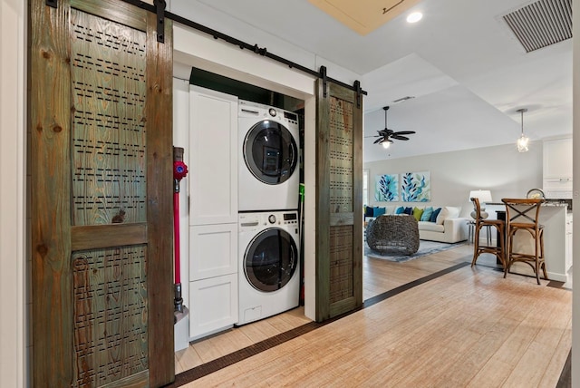 laundry area featuring light hardwood / wood-style floors, stacked washer and clothes dryer, ceiling fan, and a barn door