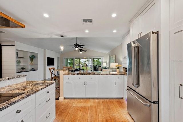 kitchen with white cabinets, vaulted ceiling, dark stone counters, and stainless steel fridge