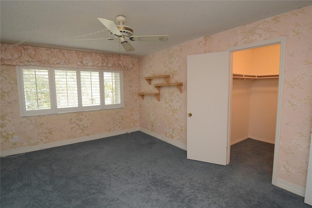 unfurnished bedroom featuring dark carpet, a closet, ceiling fan, and a walk in closet