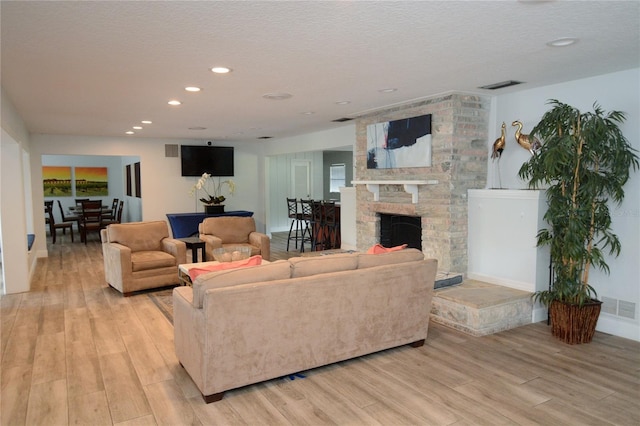 living room featuring a large fireplace, a textured ceiling, and light wood-type flooring