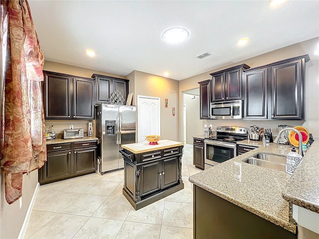 kitchen with light tile patterned floors, stainless steel appliances, dark brown cabinetry, and sink