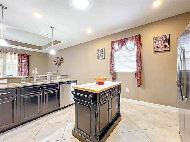 kitchen with stainless steel appliances, sink, hanging light fixtures, light stone counters, and a center island