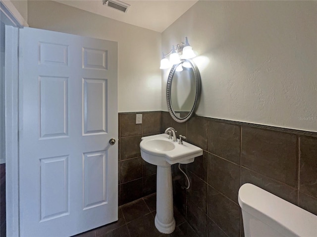 bathroom featuring toilet, tile patterned flooring, and tile walls