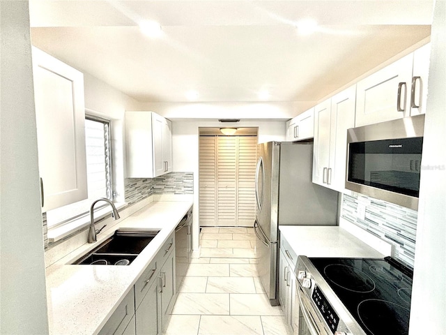 kitchen with appliances with stainless steel finishes, tasteful backsplash, white cabinets, light stone counters, and sink