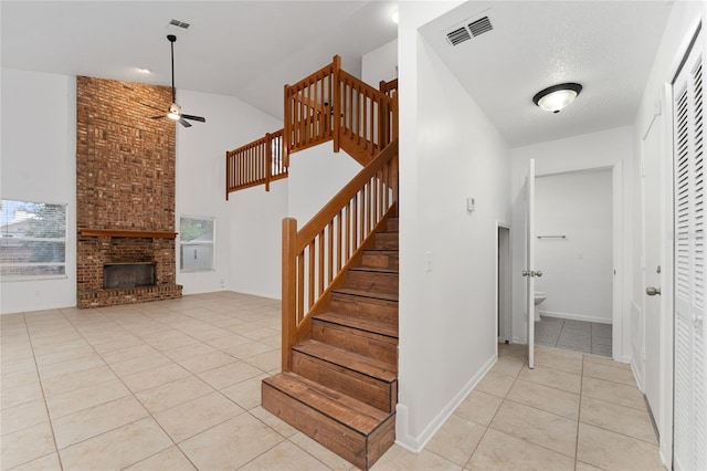 stairway with ceiling fan, lofted ceiling, tile patterned flooring, a fireplace, and a textured ceiling