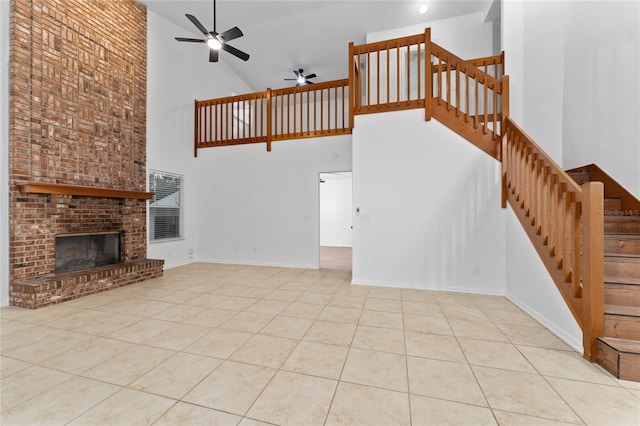 unfurnished living room featuring a fireplace, light tile patterned flooring, a towering ceiling, and ceiling fan