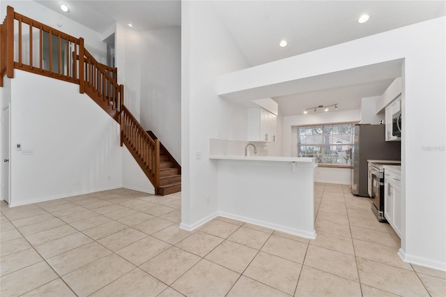 kitchen with kitchen peninsula, a kitchen bar, light tile patterned floors, appliances with stainless steel finishes, and white cabinets